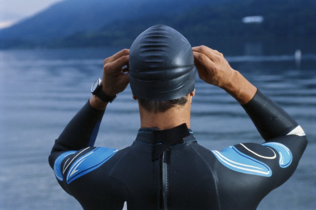 Young male triathlete adjusting swim goggles, close-up, rear view